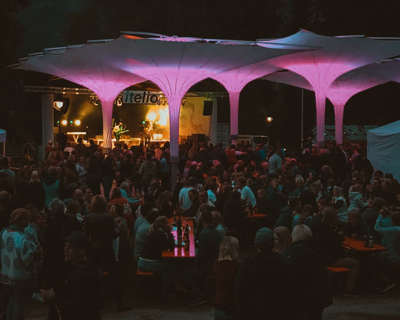 Kurpark bei Nacht mit beleuchteter Bühne und Schirmen, Gäste